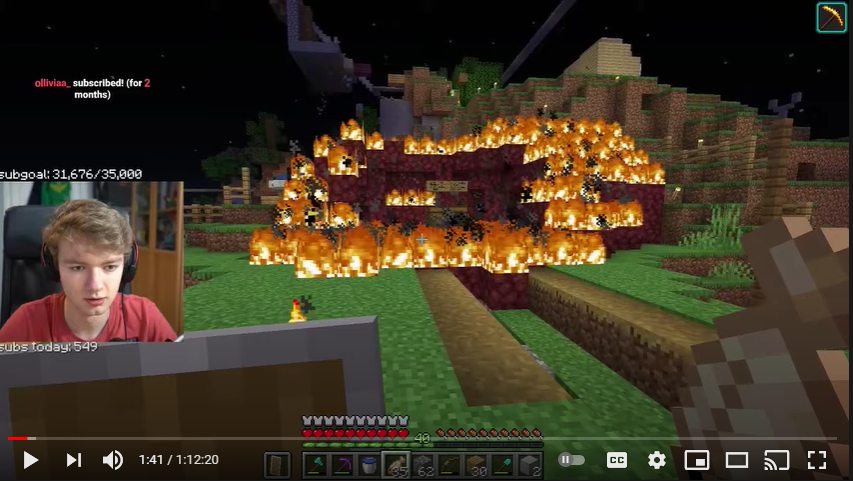 This is a screenshot from Tommy's stream. Tommy stands outside his dirt house except all of the blocks have been removed and replaced with maroon netherrack, including some of the hill. All of it, and some of the surrounding grass, is on fire. A single double chest sits in the flames with two oak signs on top of it. Tommy holds a shield and a fish in his hands and his facecam shows him genuinely shocked.